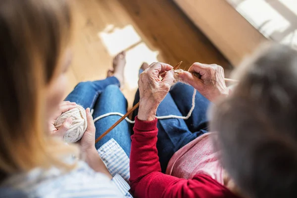 Een onherkenbaar bejaarde oma en volwassen kleindochter thuis, breien. — Stockfoto