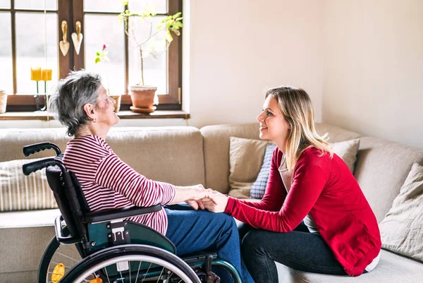 En eldre bestemor i rullestol med et voksent barnebarn hjemme . stockfoto