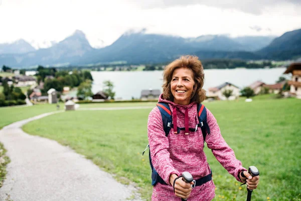 Oudere vrouw met nordic walking stokken wandelen in de natuur, rusten. — Stockfoto