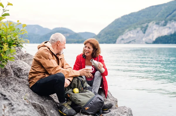Starszy emeryt para piesze wędrówki nad jeziorem w przyrodzie, siedzi i odpoczywa. — Zdjęcie stockowe