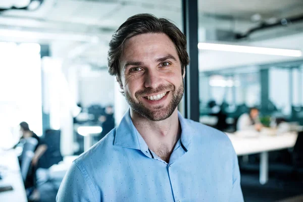 Portrait de jeune homme d'affaires debout dans un bureau, regardant la caméra . — Photo