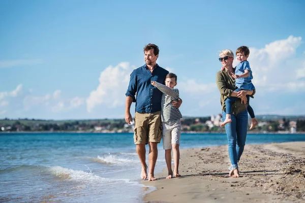 Giovane famiglia con due bambini piccoli che camminano all'aperto sulla spiaggia . — Foto Stock