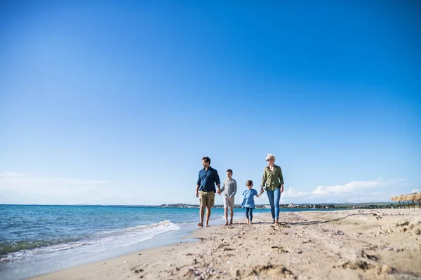 Familia joven con dos niños pequeños caminando al aire libre en la playa . — Foto de Stock