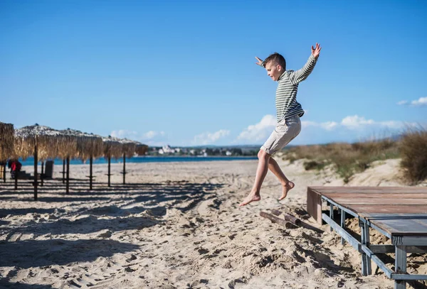 Mały chłopiec gra na zewnątrz na piasku plaży, skoki. — Zdjęcie stockowe