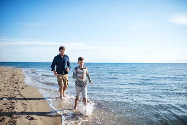 Otec s malým synem na procházce po pláži, tekoucí ve vodě. — Stock fotografie