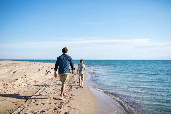 Rear melihat ayah dengan anak kecil di luar rumah di pantai, berjalan di air . — Stok Foto