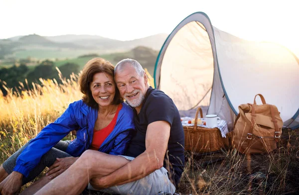 Senior tourist couple in love sitting in nature at sunset, resting. — Stock Photo, Image