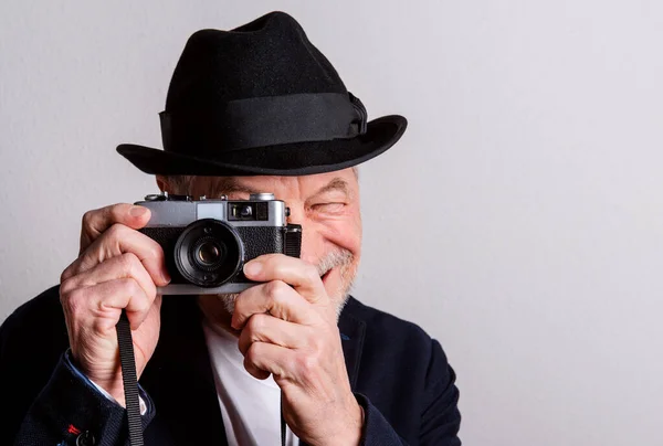 Ritratto di un anziano con cappello e macchina fotografica in uno studio, scattare foto . — Foto Stock