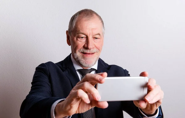 Portrait d'un homme âgé avec smartphone dans un studio, prenant selfie . — Photo