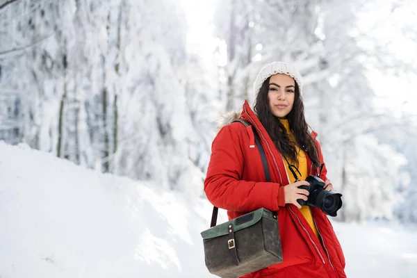 Молодая женщина с камерой стоит на улице в снегу в зимнем лесу . — стоковое фото