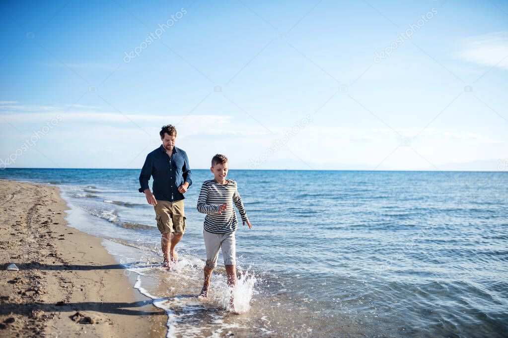 Father with small son on a walk outdoors on beach, running in water.