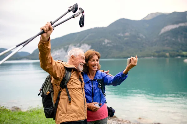Ett pensionärspar som står vid sjön i naturen och tar selfie. — Stockfoto