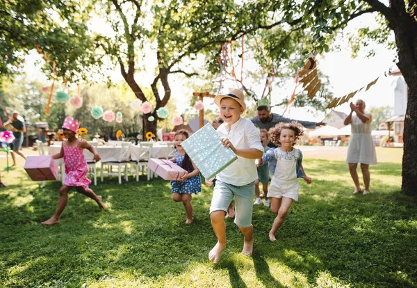 Petits enfants ruunning avec cadeau en plein air dans le jardin à la fête d'anniversaire . — Photo