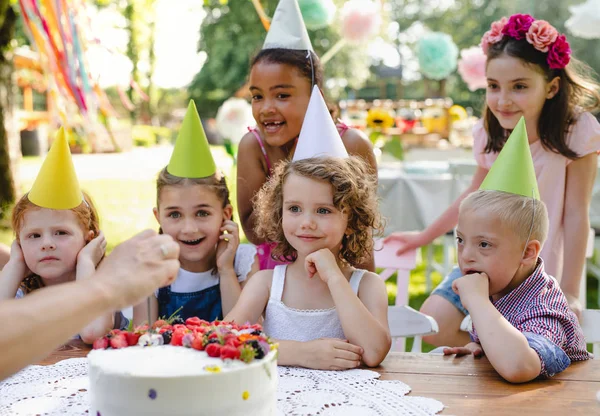 Down syndroom kind met vrienden op verjaardag feest buiten in de tuin. — Stockfoto