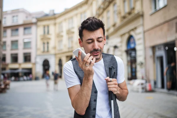 Joven ciego con teléfono inteligente en la calle en la ciudad, haciendo una llamada telefónica . —  Fotos de Stock