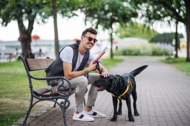 Beyaz baston ve rehber köpek şehirde parkta oturan genç kör adam.