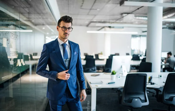 Un ritratto di un giovane uomo d'affari in piedi in un ufficio, guardando la macchina fotografica . — Foto Stock