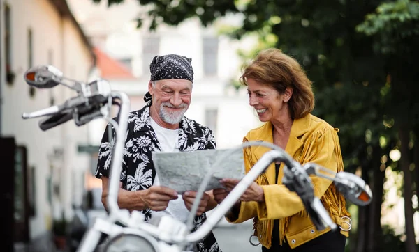 Um alegre casal de idosos viajantes com moto na cidade, olhando para o mapa . — Fotografia de Stock