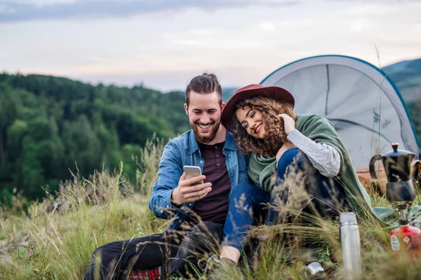 Jeunes touristes en couple avec abri de tente assis dans la nature, à l'aide d'un smartphone . — Photo