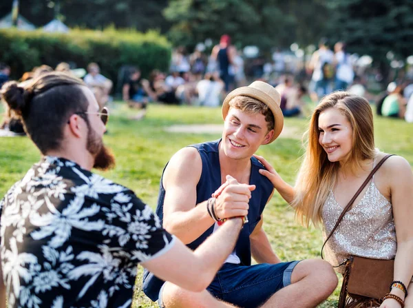 Group of young friends sitting on ground at summer festival. — Stock Photo, Image
