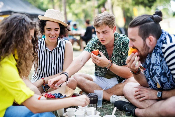 Groep jonge vrienden op het zomerfestival, zittend op de grond en etend. — Stockfoto