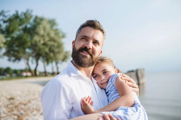 Göl kenarında oturan bir tatil baba ve küçük kızı yan görünümü. — Stok fotoğraf