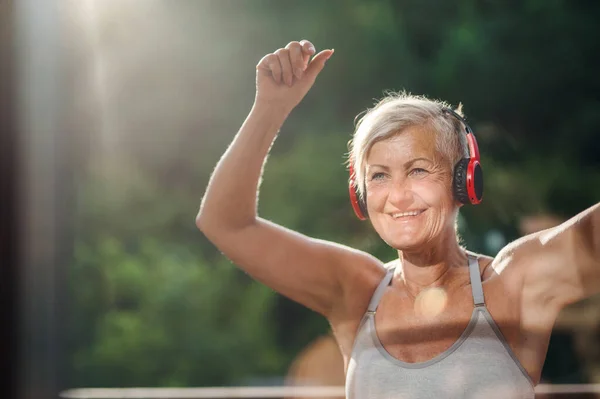 Een oudere vrouw met koptelefoon buiten op een terras in de zomer. — Stockfoto