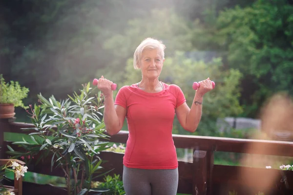 Una mujer mayor de pie al aire libre en una terraza en verano, haciendo ejercicio . — Foto de Stock