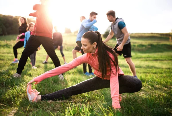 Large group of fit and active people doing exercise in nature, stretching. — Stock Photo, Image