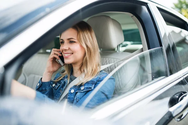 Młoda kobieta kierowca ze smartfonem siedzi w samochodzie, wykonując telefon. — Zdjęcie stockowe