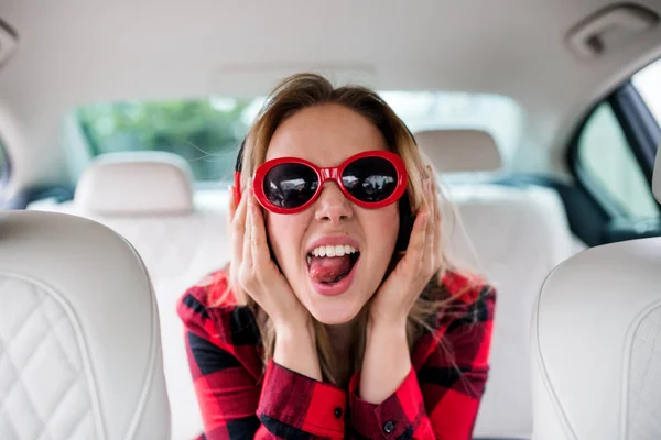 Mujer joven con gafas de sol y auriculares sentado en el coche, divertirse . — Foto de Stock