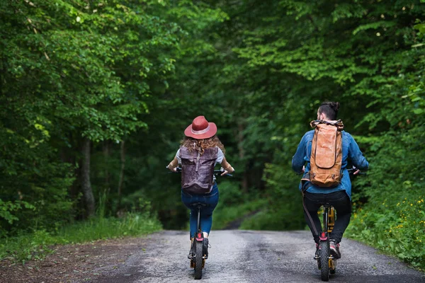 Bakifrån av unga turist par resenärer med elektriska skotrar i naturen. — Stockfoto