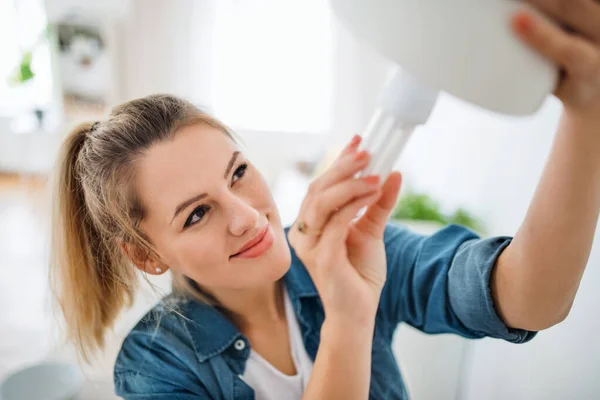 Jonge vrouw binnen thuis, gloeilamp vervangen. — Stockfoto