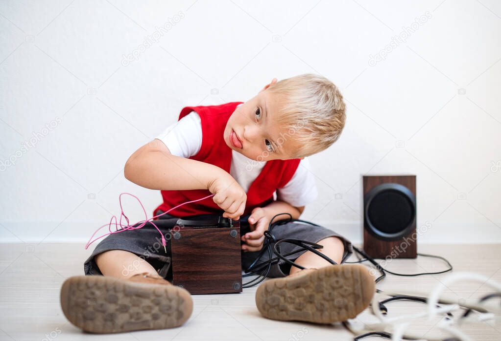 A portrait of down-syndrome school boy sitting on the floor, using loudspeakers.