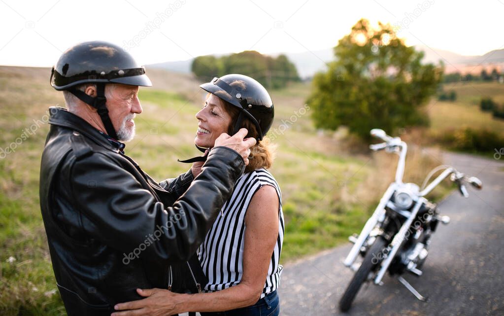 A cheerful senior couple travellers in love with motorbike in countryside.