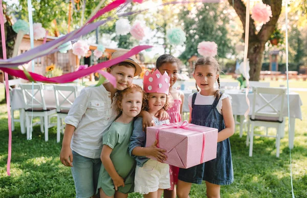 Retrato de menina pequena com amigos e presente ao ar livre no jardim no verão . — Fotografia de Stock