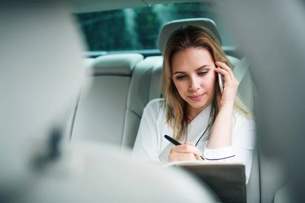 Mujer de negocios con teléfono inteligente sentado en los asientos traseros en coche de taxi . — Foto de Stock