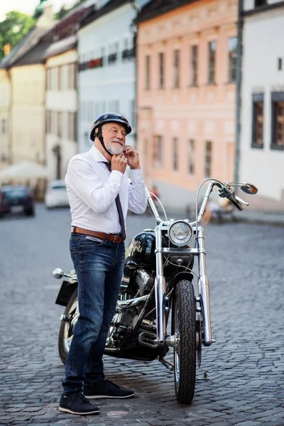 Ein älterer Geschäftsmann mit Motorrad in der Stadt, der sich einen Helm aufsetzt. — Stockfoto