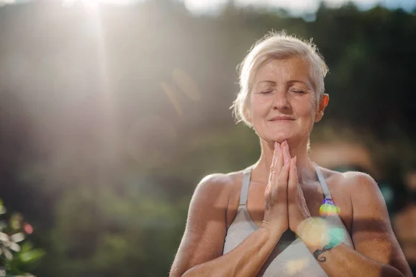 Een oudere vrouw die in de zomer buiten op een terras staat, yoga doet. — Stockfoto