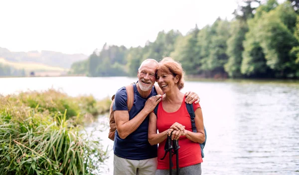 Pareja de turistas mayores en un paseo por la naturaleza, de pie junto al lago . — Foto de Stock