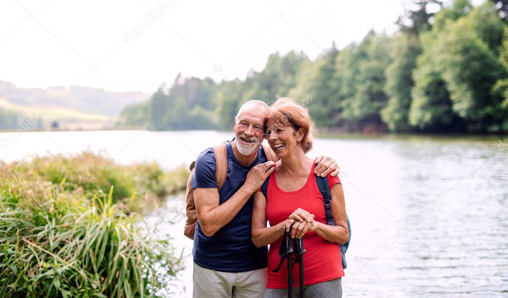Senior tourist couple on a walk in nature, standing by lake.