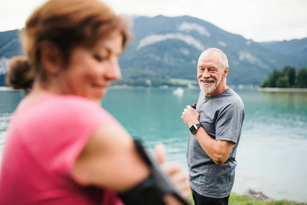 Pensionista sênior casal corredores com smartphone por lago na natureza . — Fotografia de Stock