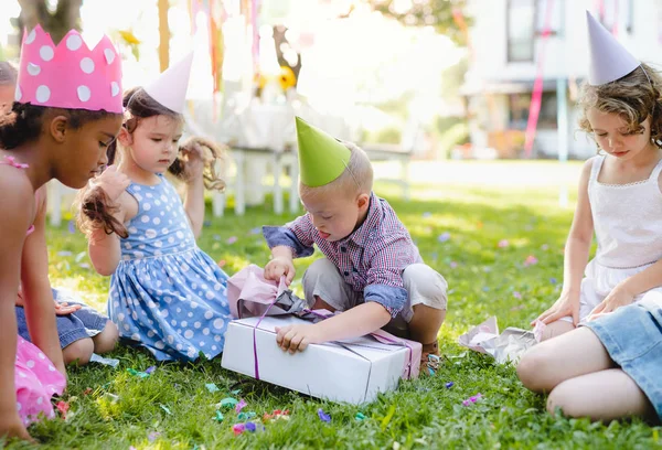 Down sindrome bambino con gli amici sulla festa di compleanno all'aperto, regali di apertura . — Foto Stock
