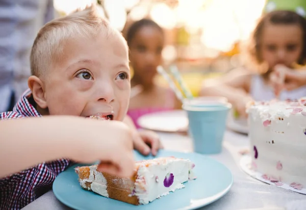 Sindrome di Down bambino con gli amici sulla festa di compleanno all'aperto, mangiare . — Foto Stock