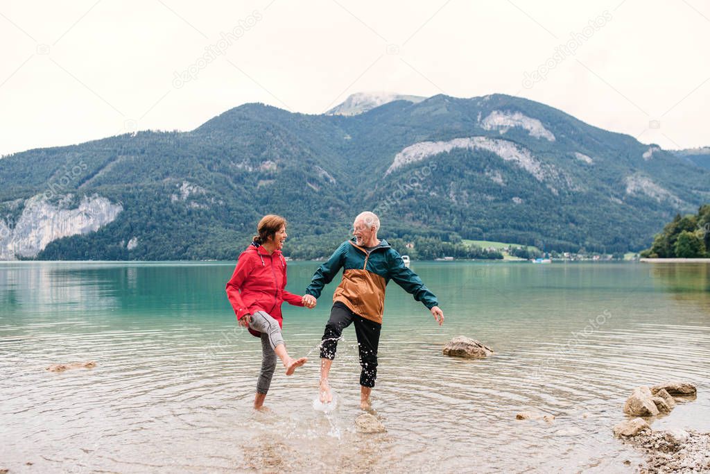 A senior pensioner couple hikers standing barefoot in lake in nature.