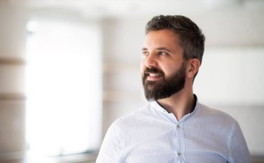 Evin içinde duran beyaz gömlekli olgun bir adamın portresi..