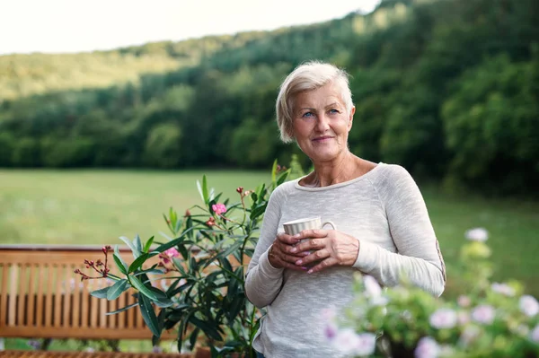 Mulher sênior com café em pé ao ar livre em um terraço no verão . — Fotografia de Stock