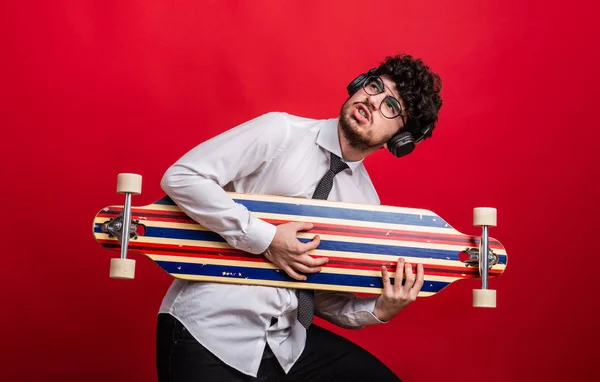 Giovane con cuffie e longboard in studio su sfondo rosso . — Foto Stock