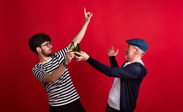 Young man and senior father with bottles in a studio on red background. — Stock Photo, Image