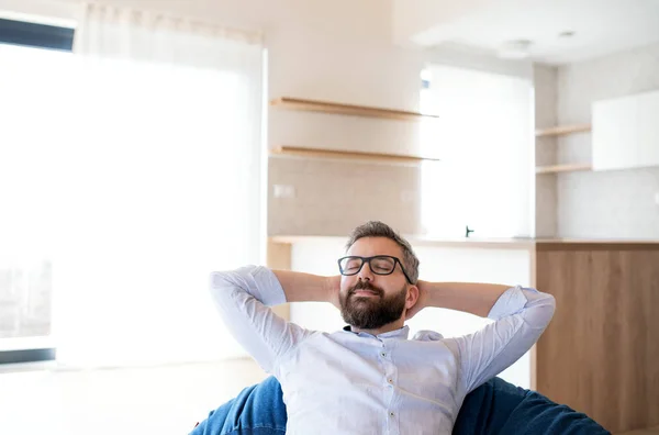 Heureux homme mature se déplaçant dans une nouvelle maison non meublée, assis sur un sac de haricots . — Photo